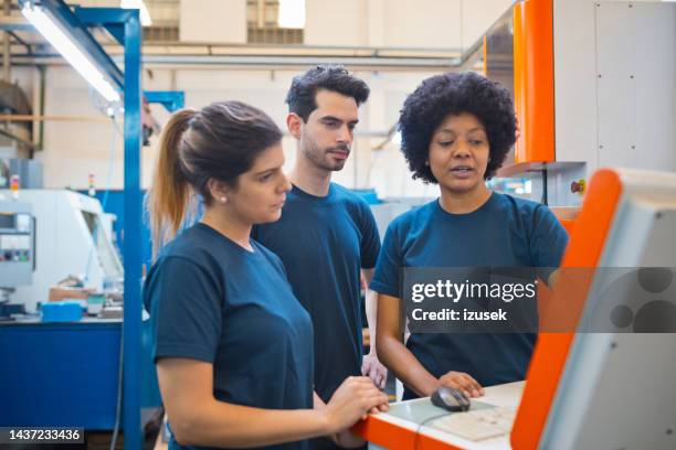 female engineer discussing over computer with male and female colleagues in factory - stem stock pictures, royalty-free photos & images