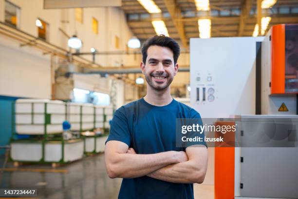 portrait of happy male blue-collar worker standing with arms crossed in factory - factory workers stockfoto's en -beelden