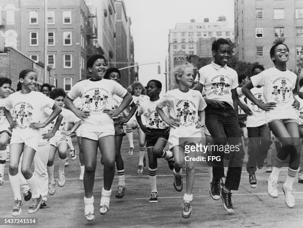 Multiracial group of children, each wearing an 'Operation Friend 24th Precinct' t-shirt an image of Mr Peanut lifting weights between two children,...