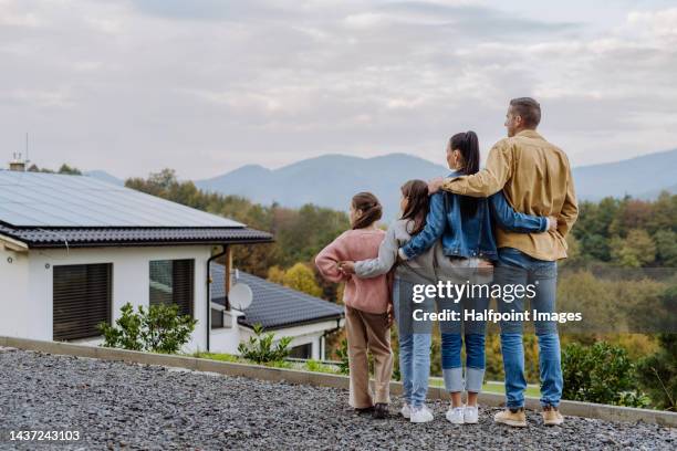 cheerful family standing and looking at their house with solar panels. alternative energy, saving resources and sustainable lifestyle concept. - large family stock photos et images de collection