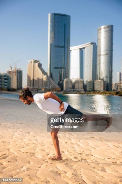 man doing yoga by the sea in abu dhabi leaning forward on one leg with hands on hips - yoga office arab stock pictures, royalty-free photos & images