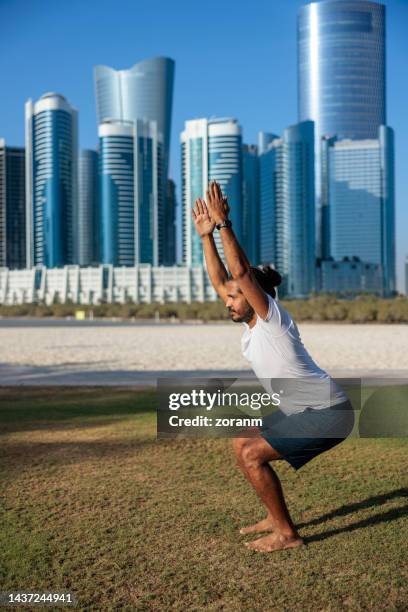 bearded man doing yoga on lawn in public park in abu dhabi squatting in chair pose - yoga office arab stock pictures, royalty-free photos & images