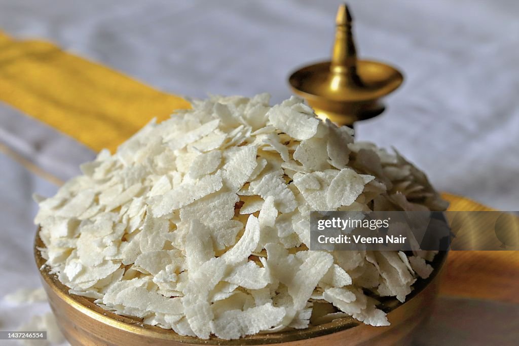 Close-up of raw poha/beaten rice/flattened rice in a brass Uruli/ brass oil lamp