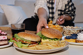 Overweight woman taking burger at home, closeup
