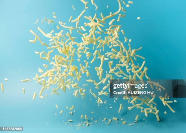 shredded mozzarella cheese flying in air on blue background - grated cheese stock pictures, royalty-free photos & images