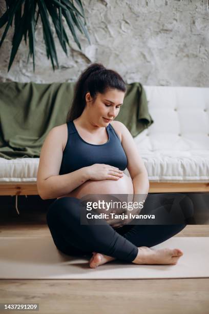 pregnant woman in lotus pose doing meditation or breathing exercises for healthy pregnancy and preparing body for childbirth. young expectant mother practicing yoga at home. - schneidersitz stock-fotos und bilder
