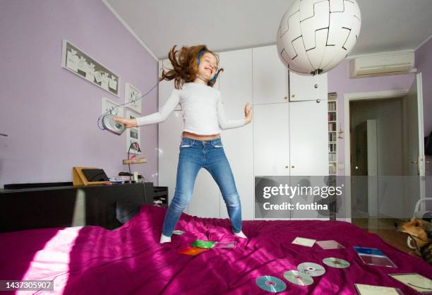 girl jumping on the bed and listening to music with cd player - bedroom radio stockfoto's en -beelden