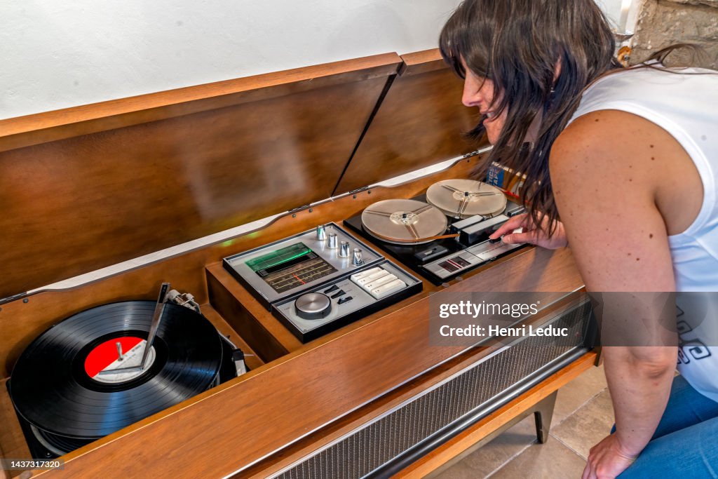 Young woman plays an LP record on an outdated mid century hi-fi stereo console wooden furniture