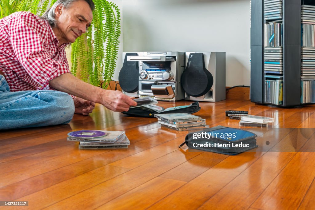 Middle age man looking at Cd's at home with his audio compact Mini Hi-Fi Stereo System in background
