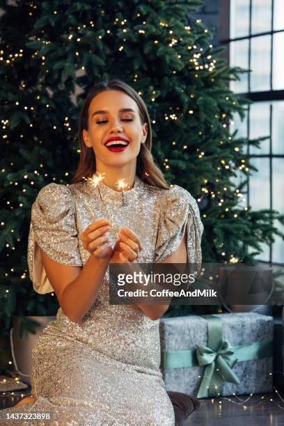 happy beautiful woman holding festive sparkler among christmas atmosphere - christmas party dress stockfoto's en -beelden