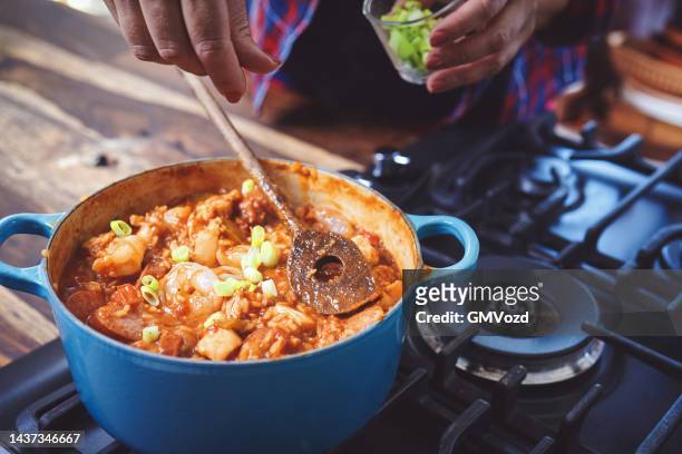 preparing cajun style chicken, shrimp and sausage jambalaya in a cast iron pot - chicken stew stock pictures, royalty-free photos & images