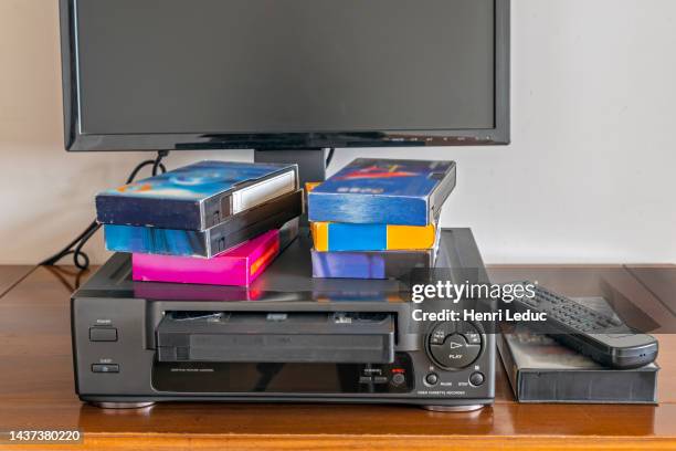 old videocassette recorder with old videotapes, tv screen and remote control placed on a wooden cabinet - 1980 television stock pictures, royalty-free photos & images