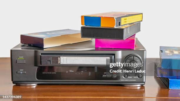 old videocassette player with old videotapes on a wooden cabinet - vcr stockfoto's en -beelden