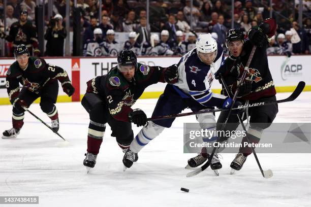 Neal Pionk of the Winnipeg Jets skates with the puck past Patrik Nemeth and Troy Stecher of the Arizona Coyotes during the third period of the NHL...