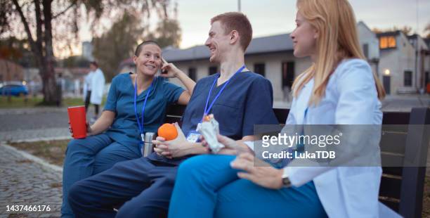 arzt und krankenschwester sitzen auf einer bank, plaudern, trinken kaffee und essen - hot nurse stock-fotos und bilder