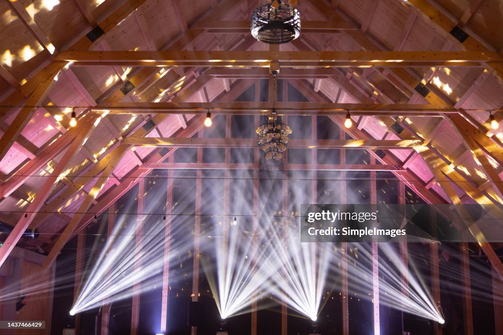 Powerful moving light beams on the ceiling structure in the interior of a public event, fashion show, concert or wedding reception.
