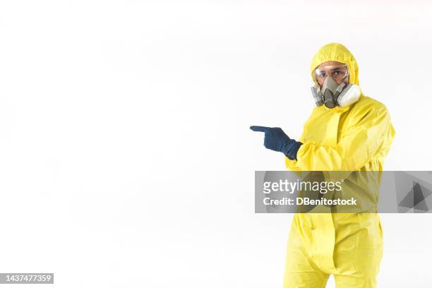 technician in a yellow nuclear protection suit, mask and protective glasses, pointing with his hands to the side, on a white background. concept of nuclear energy and pandemics. - hazmat fotografías e imágenes de stock