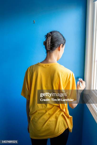 mixed race woman in yellow shirt painting a blue wall - blue shirt back stock pictures, royalty-free photos & images