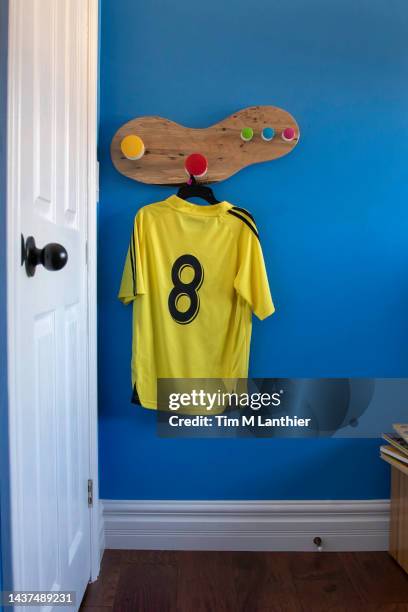 child's yellow soccer jersey hanging on hook in blue room - blank sports jersey stock pictures, royalty-free photos & images