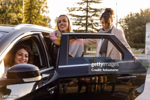 two smiling girlfriends entering the taxi via back door that came to pick them up - car pooling stock pictures, royalty-free photos & images