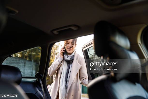 candid shot of young woman entering a car through the back door and talking on the phone - open car door stock pictures, royalty-free photos & images