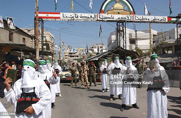 Masked Hamas supporters dressed as suicide bombers carry Korans as they march in a Hamas demonstration in Ain El Helweh Palestinian refugee camp...