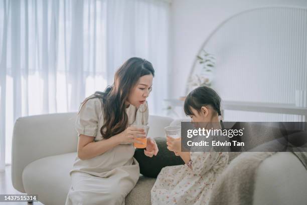 chinese pregnant mother enjoying orange juice with her daughter in living room - maternity wear stock pictures, royalty-free photos & images