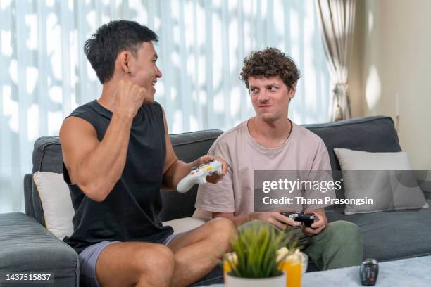 multi ethnic same sex couple playing video games at home - indian men gay stock-fotos und bilder