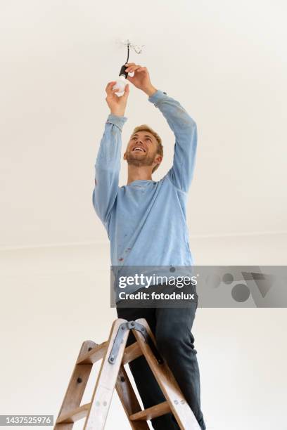 jeune homme installant une ampoule électrique du plafond du salon - led lampe photos et images de collection