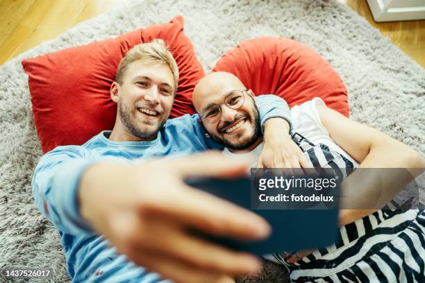 männliches paar macht selfies auf dem boden - couple smartphone stock-fotos und bilder
