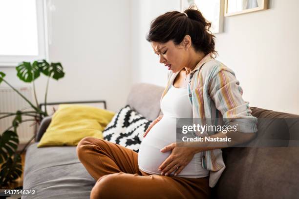 schwangere junge frau verzieht grimassen mit den händen auf dem bauch - muskelkontraktion stock-fotos und bilder
