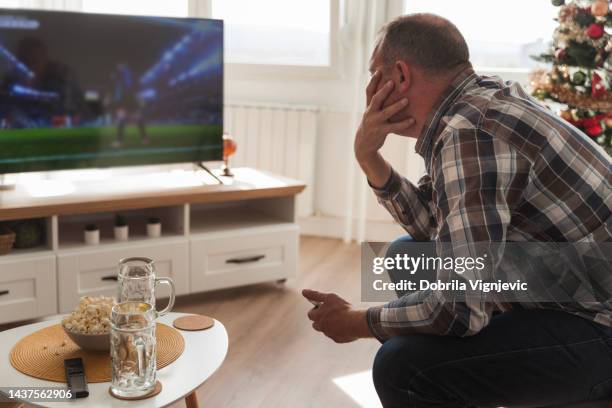 mann ruht sich zu hause aus und schaut fußball im fernsehen - online betting football stock-fotos und bilder