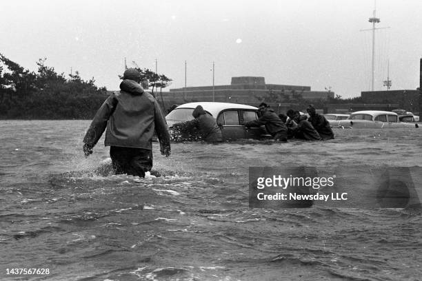 Man walks in hip deep in the parking lot of Jones Beach in Wantagh, New York, as a group pushes a car caught up in the flash flood due to Hurricane...