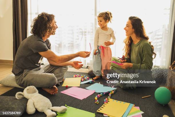cute baby girl making home decorations from color paper while sitting on carpet. - appliqué stock-fotos und bilder