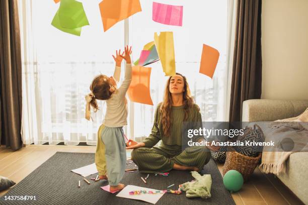 small naughty child throws colorful paper, and mom calms down and meditates. - disordinato foto e immagini stock