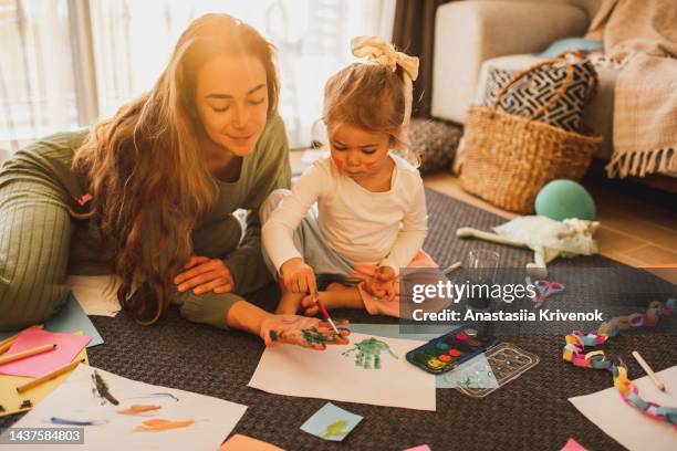 cute baby girl making home decorations from color paper while sitting on carpet. - bastelarbeit stock-fotos und bilder