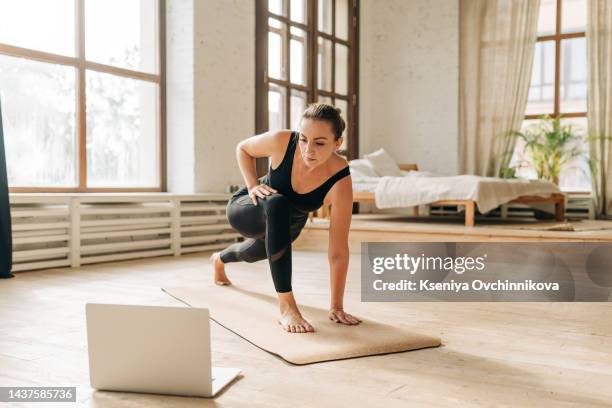 young attractive woman practicing yoga and stretching body at home using laptop for online class or virtual tutorials. girl standing in utthita parsvakonasana exercise, doing side angle pose. wellness - pilates bildbanksfoton och bilder