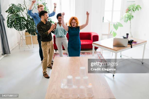 business people having fun at the office, playing office games while on a break, tearing down a pyramid of plastic cups with a  ball - sports team work stock pictures, royalty-free photos & images