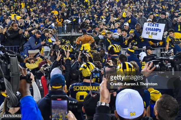 Players of the Michigan Wolverines carry the Paul Bunyan trophy into the tunnel after winning a college football game against the Michigan State...