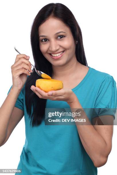 young indian woman holding ripe mango and teaspoon against white - mangoes stock pictures, royalty-free photos & images