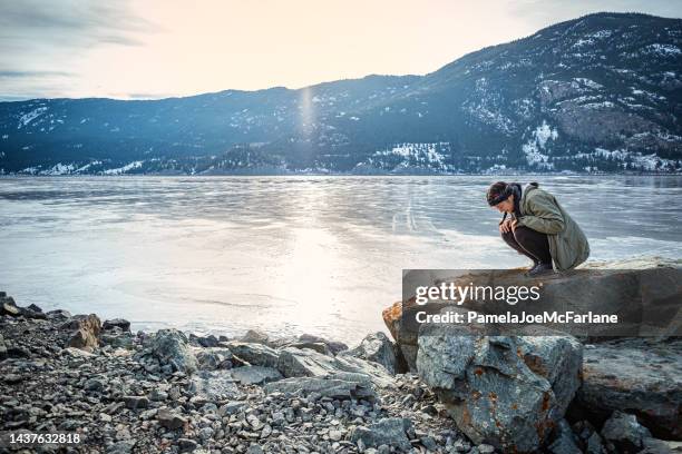 multiracial young woman examining lichen on rock at frozen lakeshore - winter testing imagens e fotografias de stock