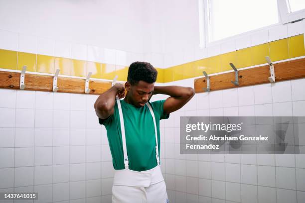 a young man putting on suspenders of fencing uniform in the locker room - mask confrontation stock pictures, royalty-free photos & images