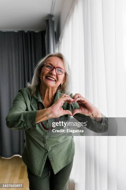 retrato de una mujer mayor en casa mostrando un símbolo en forma de corazón - human heart fotografías e imágenes de stock