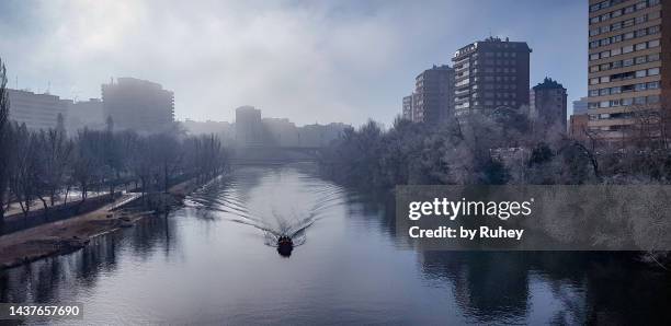 a rescue boat on the rio pisuerga as it passes through valladolid, seen from the poniente bridge on a foggy morning. - valladolid spanish city stock-fotos und bilder