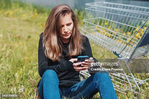 young woman worried and using phone against empty market trolley outdoor - crisis hotline stock pictures, royalty-free photos & images
