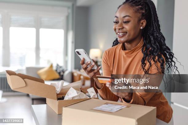 beautiful african-american woman using online paying services on smart phone - e commerce stock pictures, royalty-free photos & images