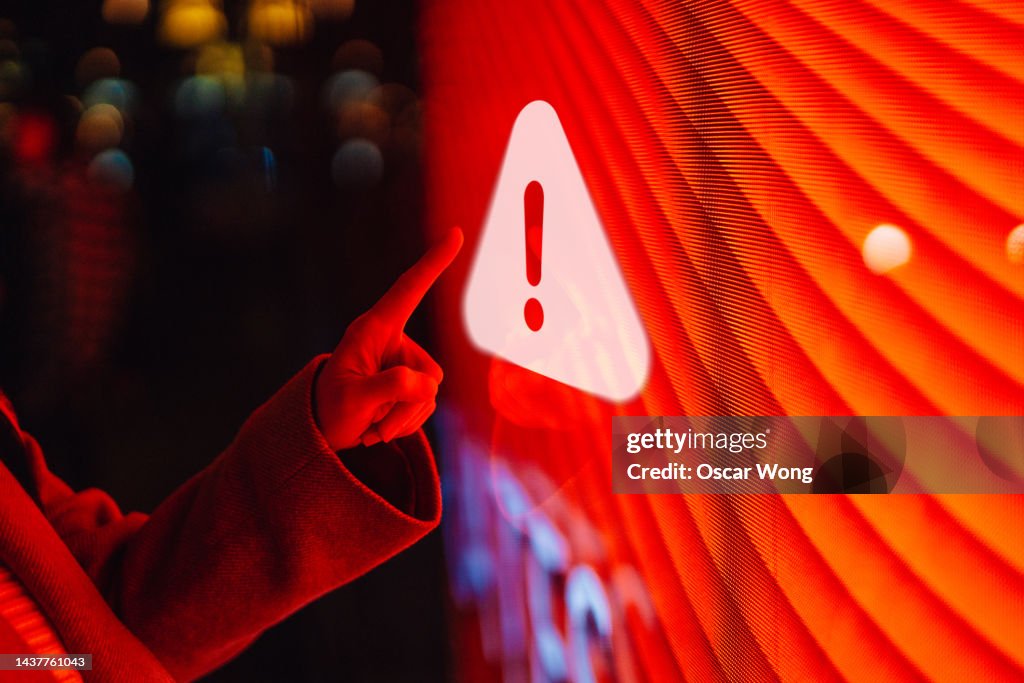 Close-up of female hand touching illuminated digital screen displaying a warning sign