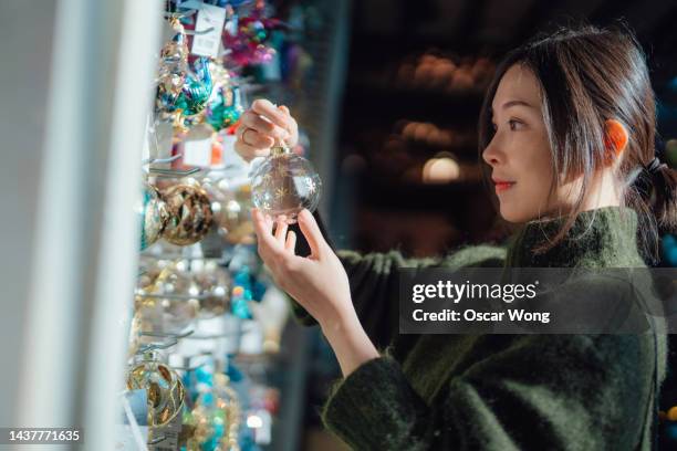 young asian woman choosing christmas baubles and ornaments at the store. - christmas decorations in store stock pictures, royalty-free photos & images