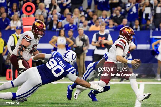 Taylor Heinicke of the Washington Commanders runs with the ball as Grover Stewart of the Indianapolis Colts dives for a tackle in the fourth quarter...