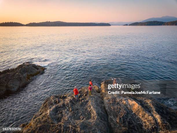 erweiterte multirassische familie mit zwei generationen, die den sonnenuntergang vom felsigen ufer aus beobachtet - vancouver island stock-fotos und bilder